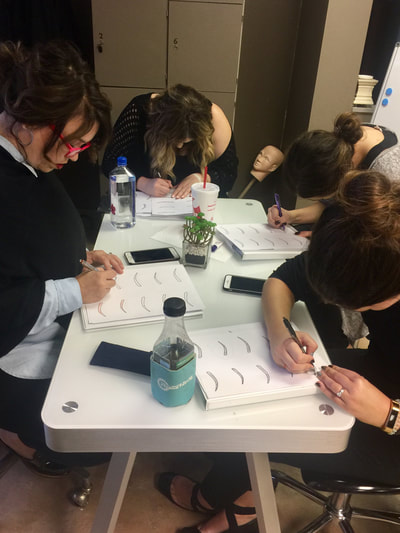 Students practicing hair stroke pattern on paper at the Academy
